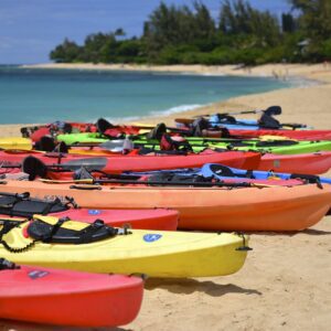 A group of kayaks on the beach near water.