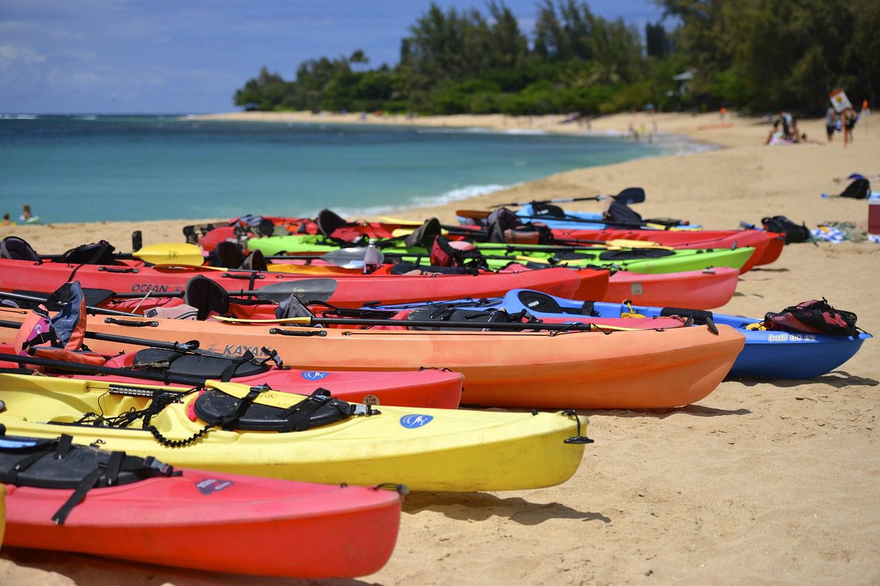 A group of kayaks on the beach near water.